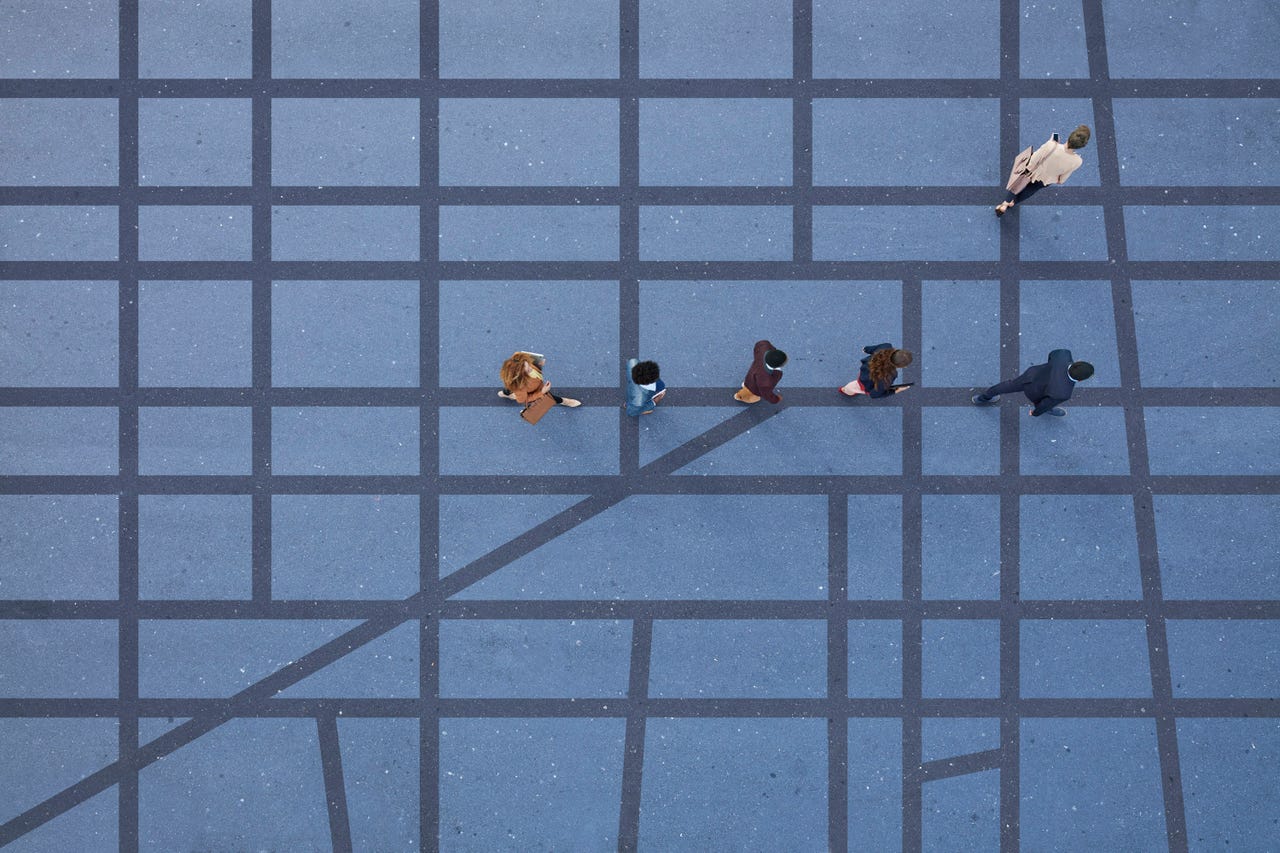 People walking in line on road, painted on asphalt, with one person walking off in different direction.