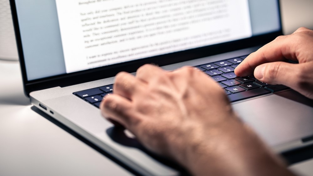 Two hands type on a laptop keyboard.