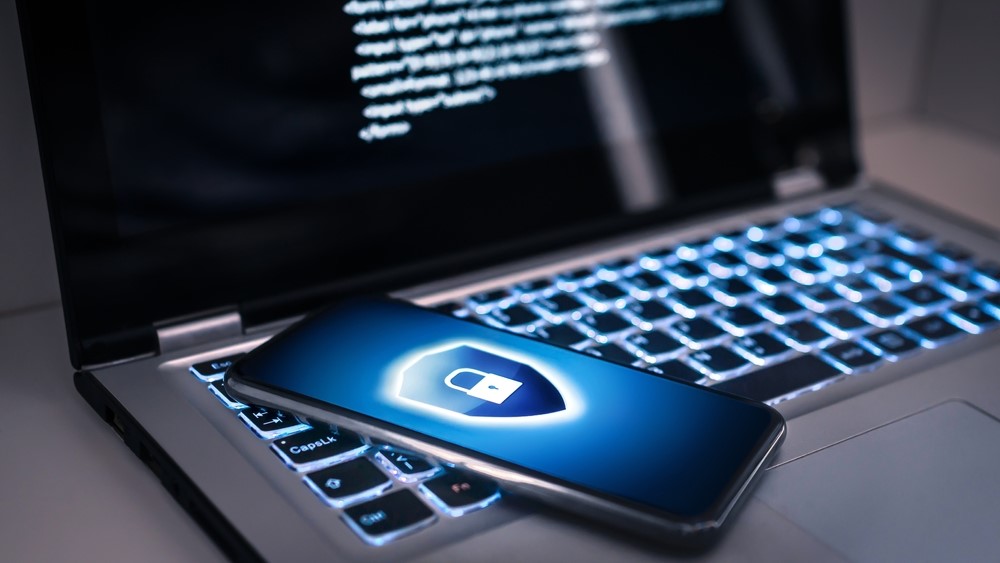 A phone with a lock symbol sits on top of a laptop keyboard that is lit up blue.