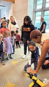 Students work with kids to touch the robot while it is off. They are in a library.