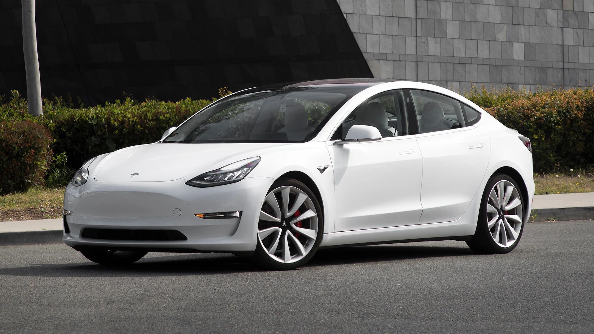 Tesla Model 3 performance white glamour shot, suburban background with grass and hedges. 