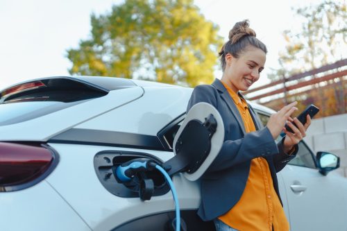 Young woman with smartphone waiting while her electric car charges