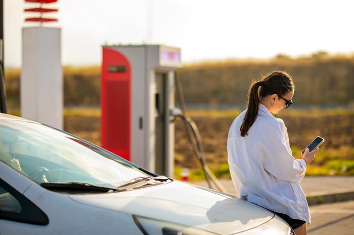 Woman looks at phone while waiting for EV to charge. 