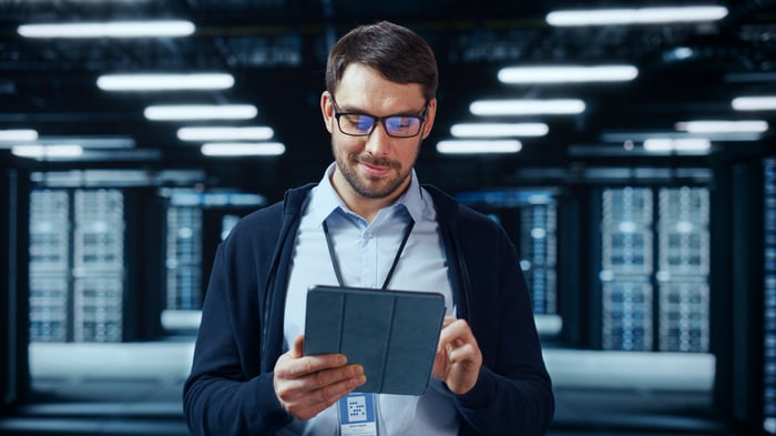 A person looking down at a tablet while standing in a data center.