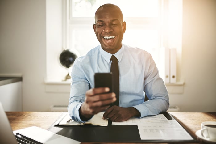 An investor smiles at something on a phone in a sunny office.