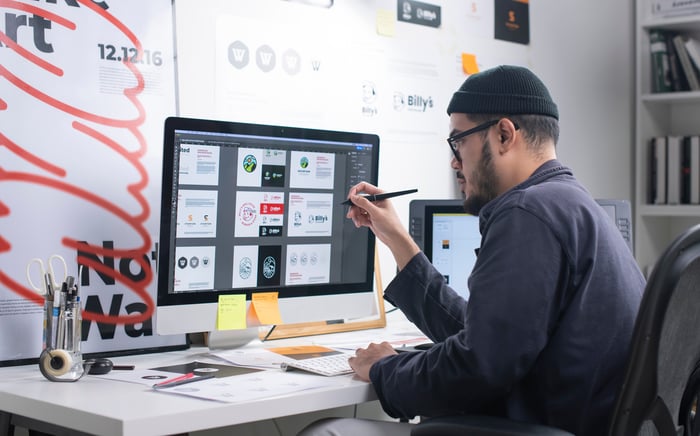 A person sits at a desktop with graphic design tools open. 