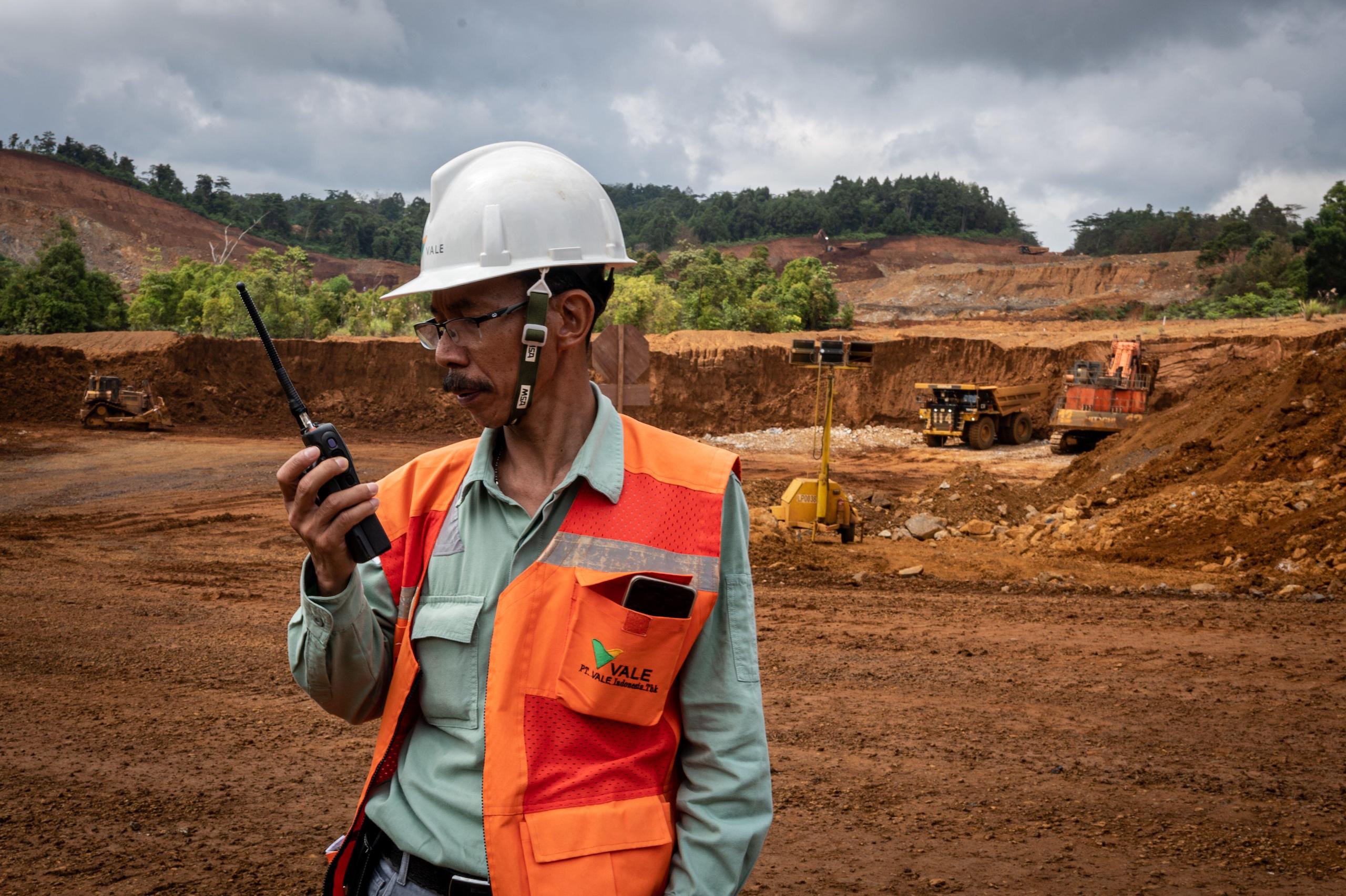 A worker in safety gear, holding a walkie-talkies  while working on a mine site