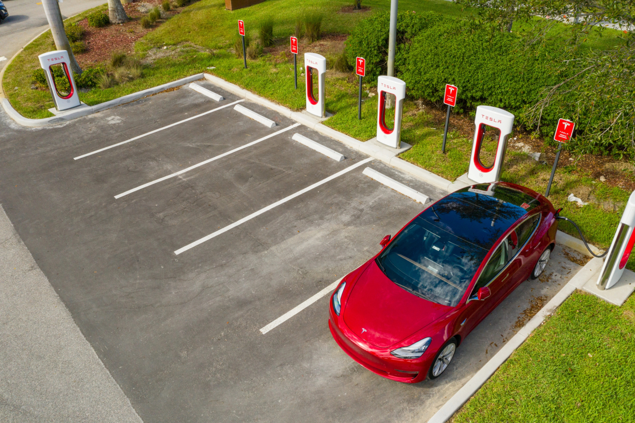 Aerial of a Red Tesla Model 3 Charging in a Tesla Supercharger, Four Empty Charging Spaces