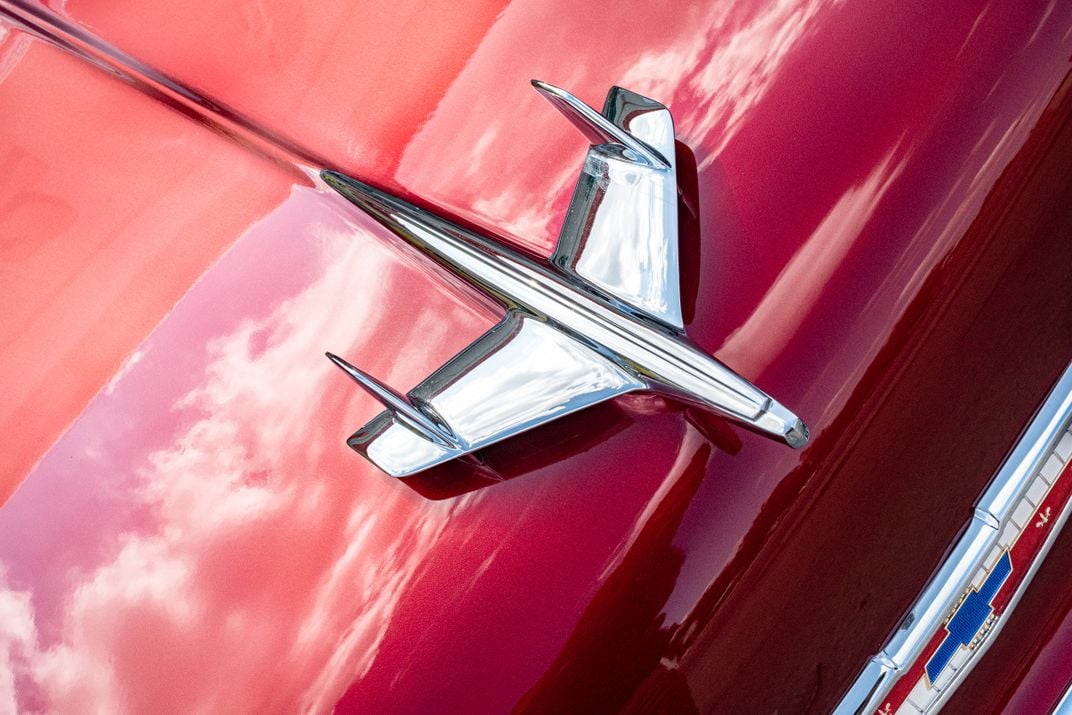 7 - An aerodynamic chrome ornament tops the hood of a cherry-red 1955 Chevy.