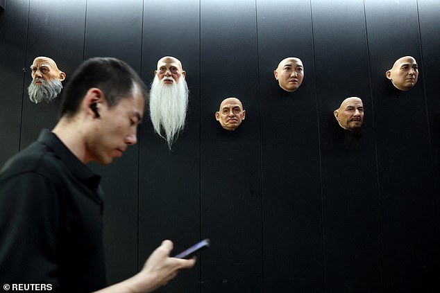 An employee checks his mobile phone as he walks past displays of robot heads at the office of humanoid robots developer Ex-Robots in Dalian