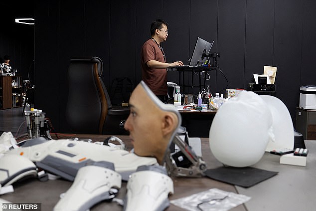 An employee works on a desk near displays of humanoid robot parts at the Ex-Robots factory