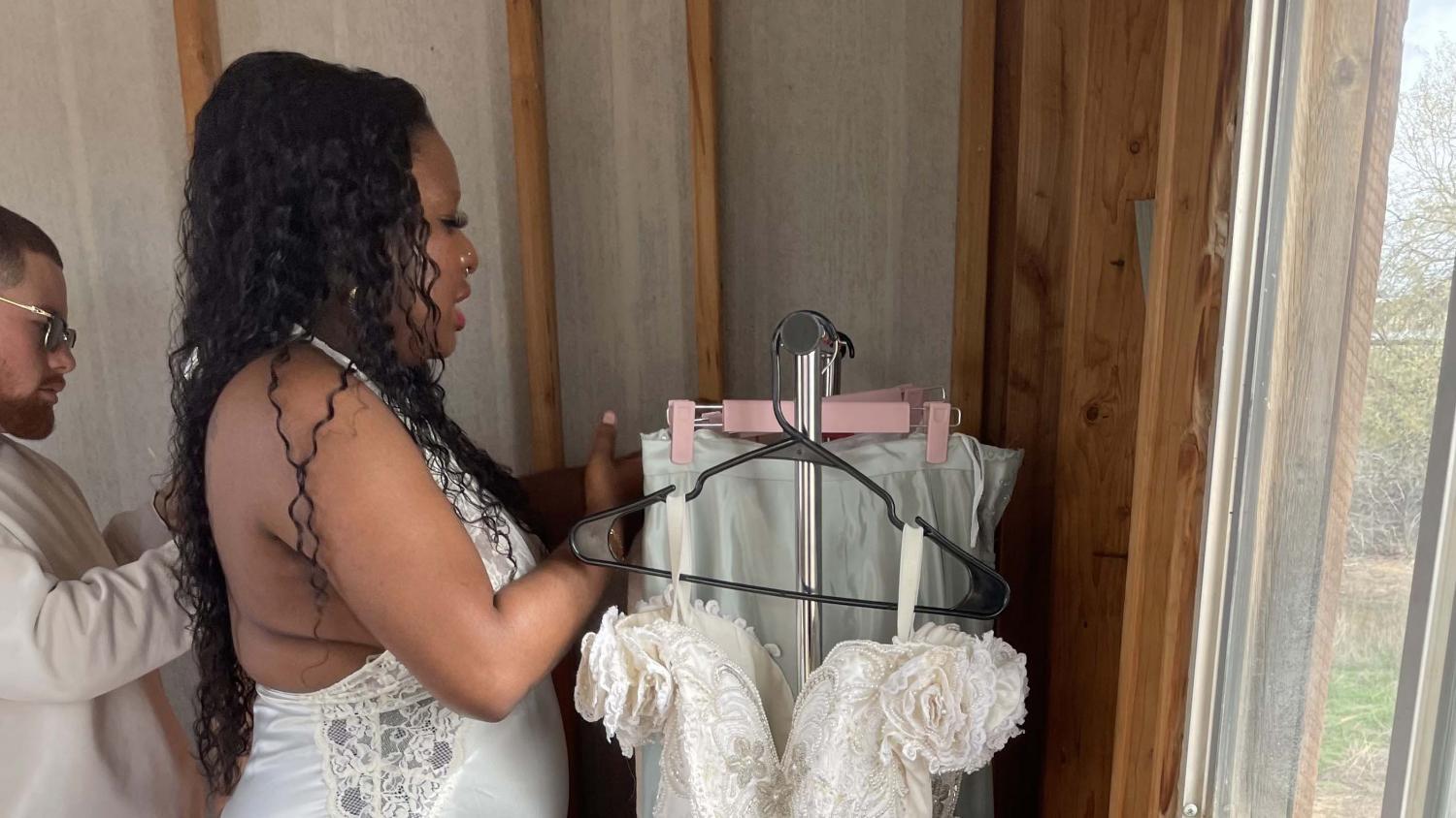 A young Black woman, Nessie Jenkins, sets up dresses on a hanging clothing rack.