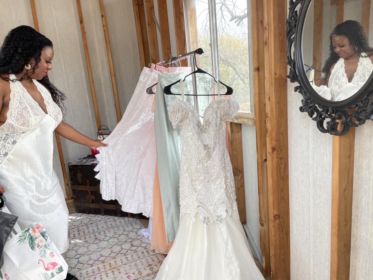 Taylor Nesiah Jenkins, a young Black woman in a white satin dress, holds a white article hanging on a clothing rack.