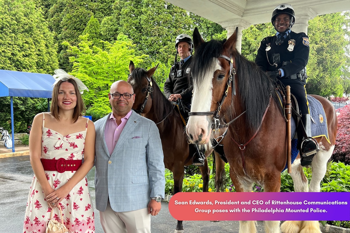 A man and woman stand in front of two mounted police officers on horses.