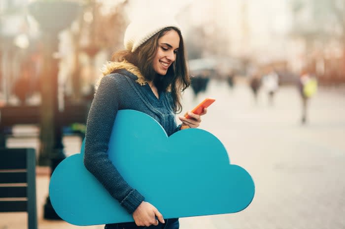 A person holds a cardboard cutout of a cloud while using a smartphone.