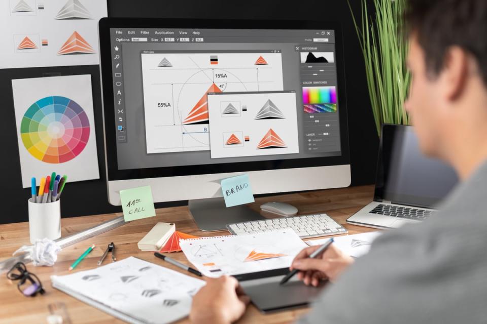 A person sitting at a desk with a desktop and various office supplies scattered across the table, many of which feature icons of various graphics and designs. 