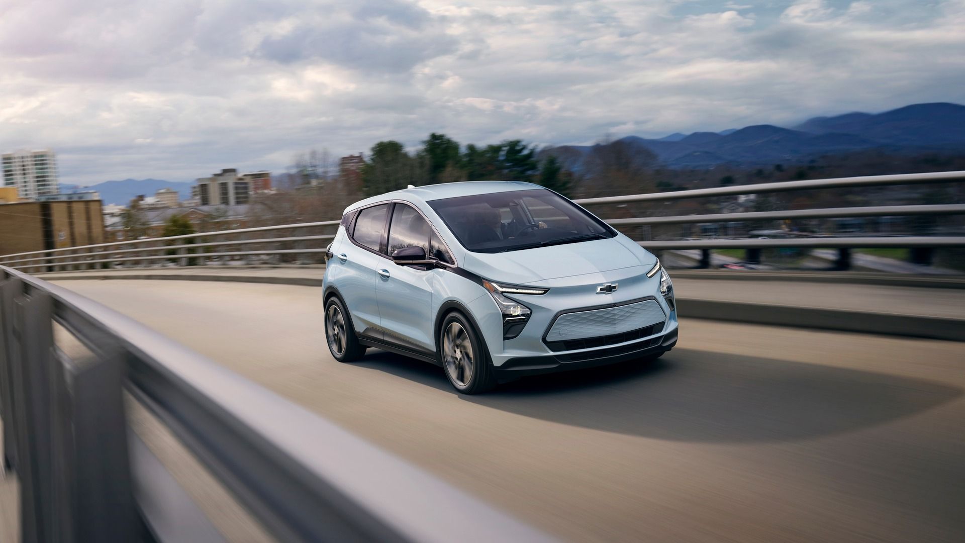 A White Chevrolet Bolt EV driving on a highway overpass.