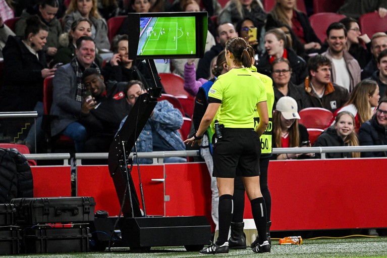 A referee reviews footage on a VAR display screen during a UEFA Champions League women's quarter-final match.