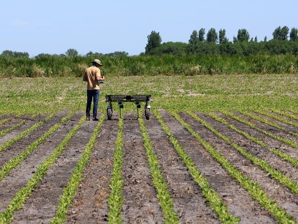 a man stands next to a small machine in a field