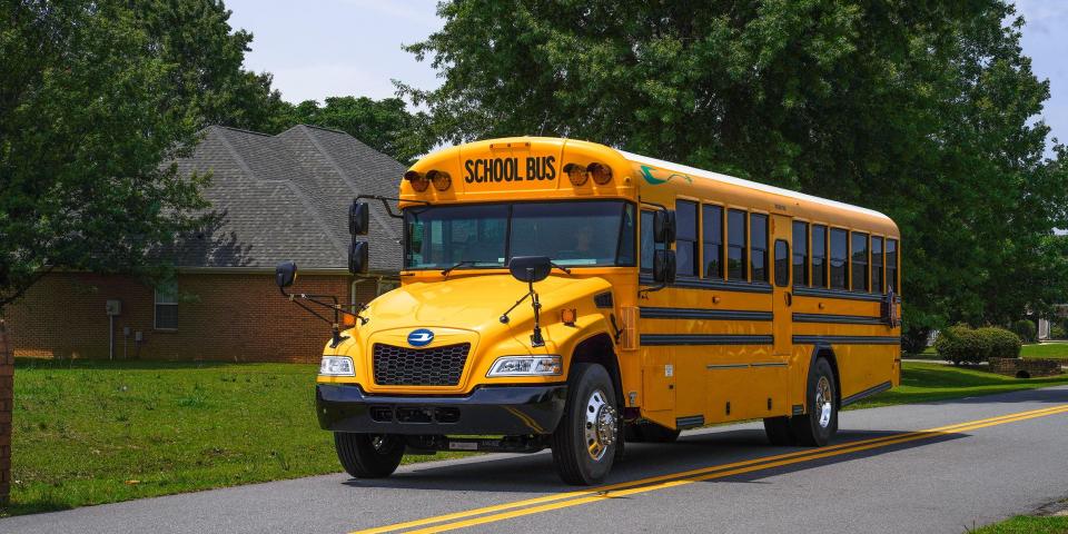 A yellow electric school bus drives down the road.