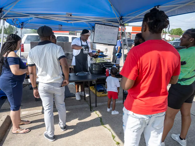 Raymond Barbour stands under a blue canopy serving his BBQ to customers.