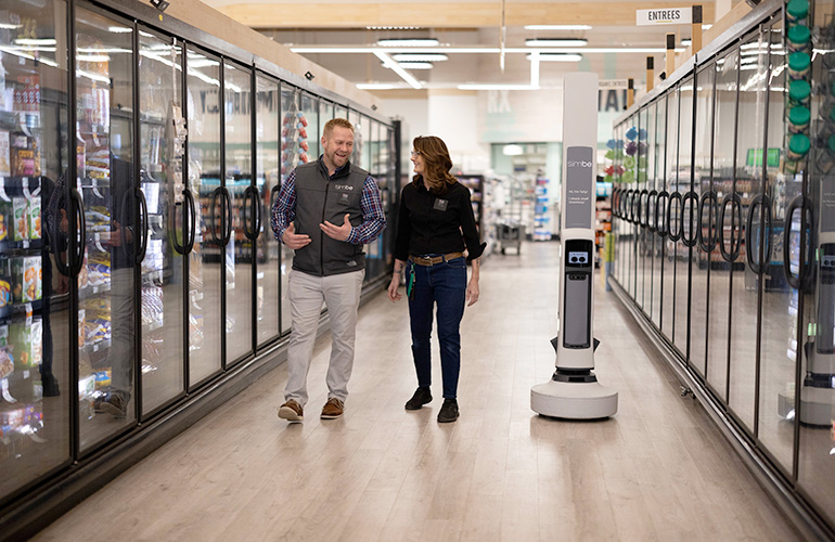 two workers walking through a store aisle next to a Tally robot.