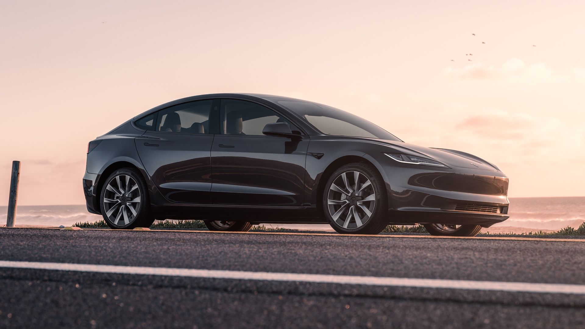 A static front-quarter shot of a gray Tesla Model 3 parked by the ocean