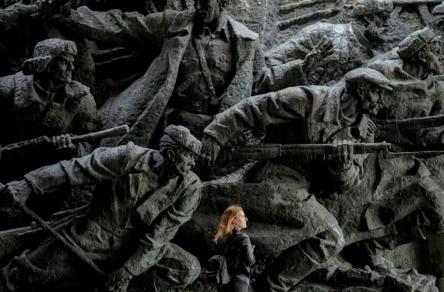 A woman walks backdropped by bas-relief sculptures depicting war scenes in the National Museum of the History of Ukraine in the Second World War in Kyiv, Ukraine, Monday, April 8, 2024. (AP Photo/Vadim Ghirda)